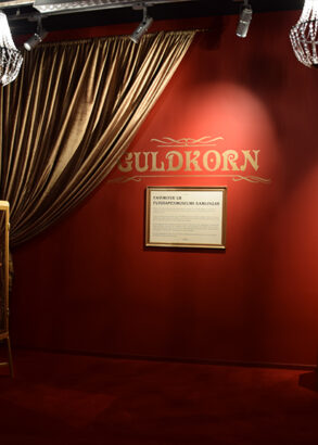 Ett r&ouml;dm&aring;lat rum med tv&aring; kristallkronor i taket. P&aring; v&auml;ggen st&aring;r det Guldkorn i guld.