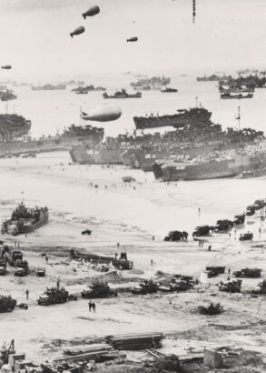 Svartvit historisk bild av Normandiestranden under D-dagen 1944. Stora landstigningsfartyg ligger vid stranden medan m&auml;ngder av milit&auml;rfordon, soldater och utrustning r&ouml;r sig i land. Himlen fylls av f&ouml;rankrade ballonger och horisonten av fartyg.