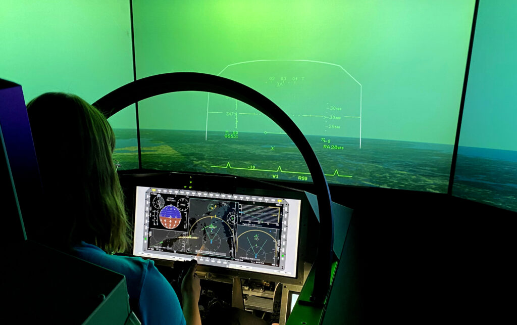 En kvinna sitter som i en cockpit med en stor skärm under provflygningen av JAS 39 Gripen E-simulator