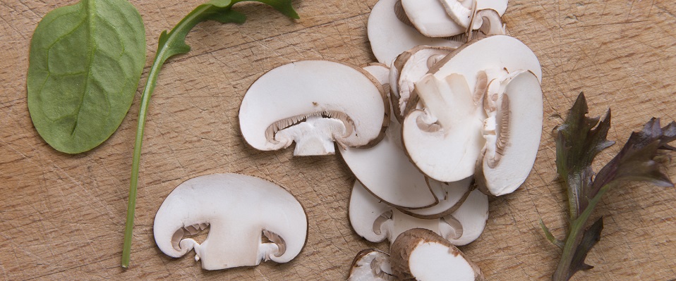 Råvaror från köket, spenat, ruccola och skivade champinjoner på en skärbräda av trä