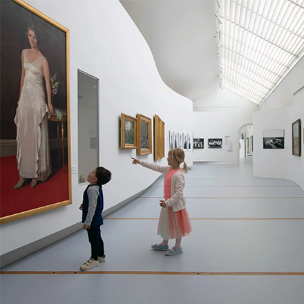 Tv&aring; barn tittar och pekar p&aring; en av m&aring;nga tavlor i en vit korridor.